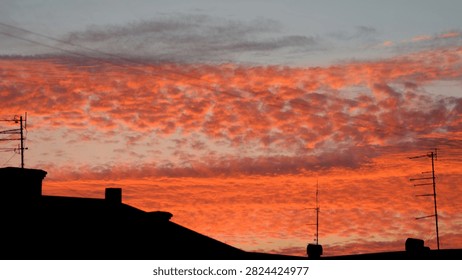 Dramatic orange sunset clouds over dark city rooftop silhouettes with antennas, evening sky background Photo.