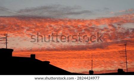 Dramatic orange sunset clouds over dark city rooftop silhouettes with antennas, evening sky background Photo.