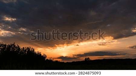 Dramatic Orange Sunset with Dark Storm Clouds and Sun Rays Above Tree Silhouettes