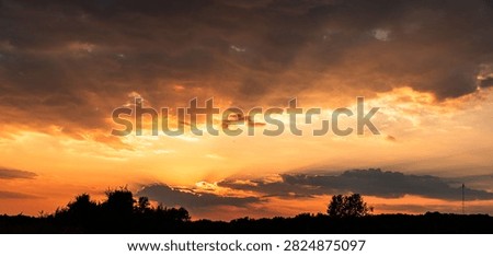 Dramatic Orange Sunset with Dark Storm Clouds and Sun Rays Above Tree Silhouettes