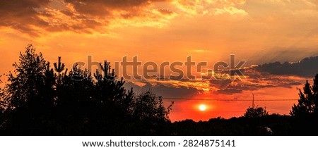 Dramatic Orange Sunset with Dark Storm Clouds and Sun Rays Above Tree Silhouettes