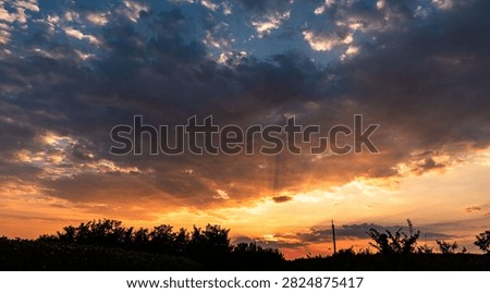 Dramatic Orange Sunset with Dark Storm Clouds and Sun Rays Above Tree Silhouettes