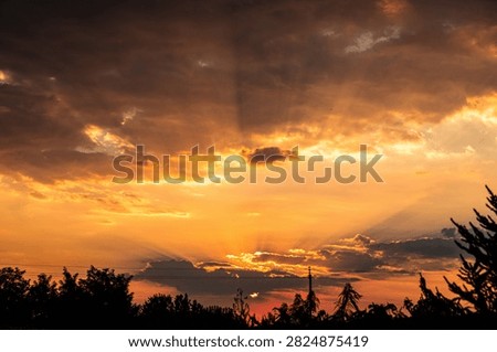 Dramatic Orange Sunset with Dark Storm Clouds and Sun Rays Above Tree Silhouettes