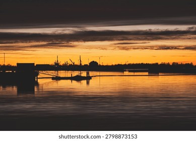Dramatic orange sunset over Noblessneri port in Tallinn, Estonia, with industrial crane silhouettes reflecting beautifully on the calm sea water.