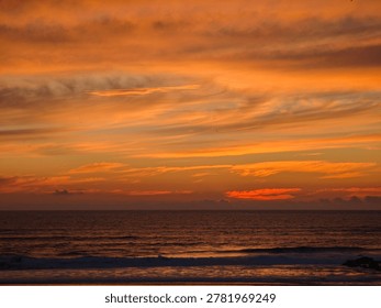 Dramatic orange sunset over the ocean with calm waves and vivid evening clouds.