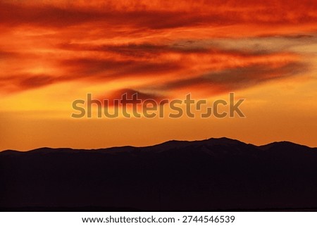 Dramatic orange sunset sky over mountain silhouette.