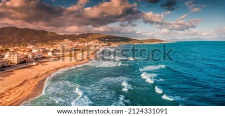 Dramatic panoramic aerial view of iconic Sarti resort town and famous long and empty sandy beach at sunset time with high waves. Vacation on Halkidiki, Greece