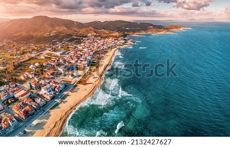Dramatic panoramic aerial view of iconic Sarti resort town and famous long and empty sandy beach at sunset time with high waves. Vacation on Halkidiki, Greece