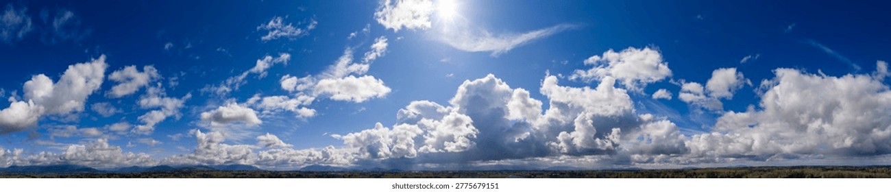 Dramatic panoramic cloudscape in British Columbia, Canada, featuring sunlit blue sky, towering cumulus clouds and rolling landscape.