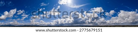 Dramatic panoramic cloudscape in British Columbia, Canada, featuring sunlit blue sky, towering cumulus clouds and rolling landscape.