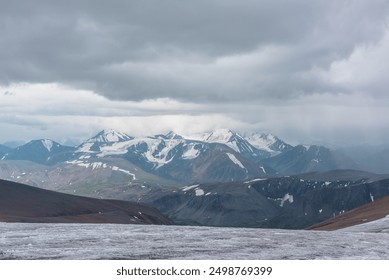 Dramatic panoramic view from big glacier to wide alpine valley and large snow-capped mountain range in rainy low clouds. Awesome vast landscape with high snowy mountains in rain under gray cloudy sky.