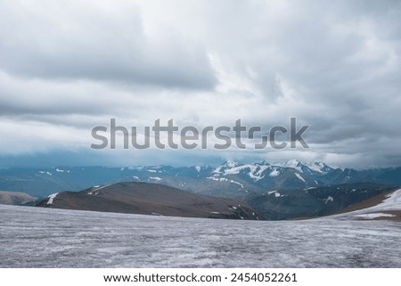 Dramatic panoramic view from big glacier to wide alpine valley and large snow-capped mountain range in rainy low clouds. Awesome vast landscape with high snowy mountains in rain under gray cloudy sky.