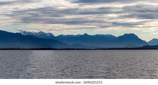Dramatic panoramic view over the dark waters of Lake Constance (Bodensee) near Lindau, Germany, with the silhouette of the Swiss or Austrian Alps beneath a cloudy, moody sky
