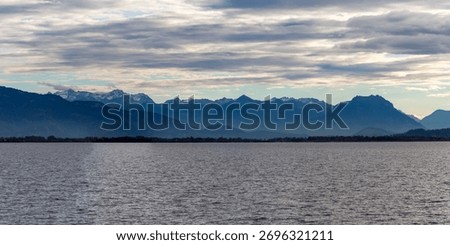 Dramatic panoramic view over the dark waters of Lake Constance (Bodensee) near Lindau, Germany, with the silhouette of the Swiss or Austrian Alps beneath a cloudy, moody sky