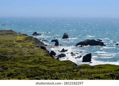 Dramatic panoramic view of the rugged California coastline, featuring sheer cliffs, majestic sea stacks, and a winding trail for hiking adventures.