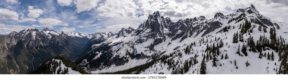 Dramatic panoramic view of snow-capped peaks, alpine forest and a deep valley in British Columbia, Canada.