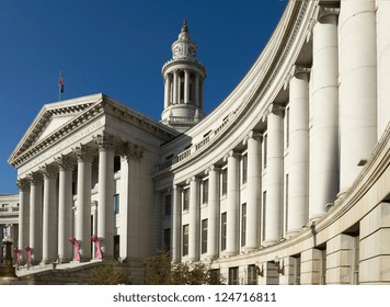 Dramatic perspective of The City and County Building in Denver, Colorado, under a blue sky. The building is adorned with pink Breast Cancer Awareness ribbons.