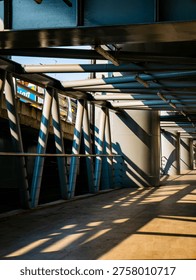 Dramatic perspective of an empty elevated walkway with steel tube roof structure casting striped shadows in golden morning light