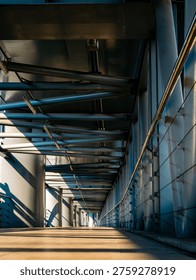 Dramatic perspective of an empty elevated walkway with steel tube roof structure casting striped shadows in golden morning light