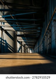 Dramatic perspective of an empty elevated walkway with steel tube roof structure casting striped shadows in golden morning light