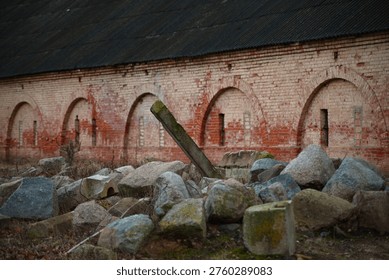 A dramatic perspective shot looking down the length of a long, historic red brick wall. The structure is defined by a rhythmic series of tall, arched decorative niches. The weathered bricks show a rich texture of age, standing above a traditional cobblestone base under the soft, muted light of an overcast evening.