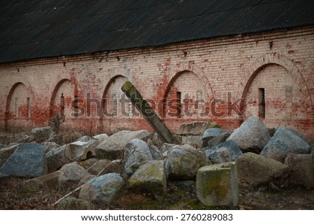 A dramatic perspective shot looking down the length of a long, historic red brick wall. The structure is defined by a rhythmic series of tall, arched decorative niches. The weathered bricks show a rich texture of age, standing above a traditional cobblestone base under the soft, muted light of an overcast evening.
