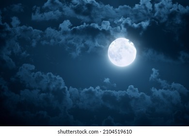 Dramatic photo illustration of a nighttime sky with brightly lit clouds and large, bright full moon would make a great background. - Shutterstock ID 2104519610
