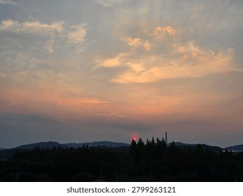 Dramatic pink sun setting over pine trees with misty mountains in the background