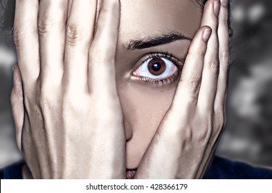 Dramatic Portrait. Concept Of Anxiety And Fear. Intense Look Through The Hands Covering The Face.