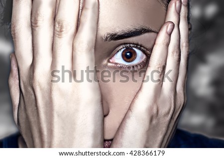 Dramatic portrait. Concept of anxiety and fear. Intense look through the hands covering the face.