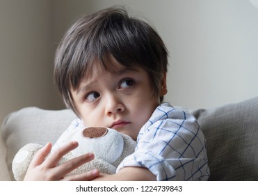 Dramatic portrait of little boy sittingon sofa and cuddling teddy bear with scared face,Unhappy Child sitting alone and looking out with worrying face,Toddler boy on corner punishment sitting.