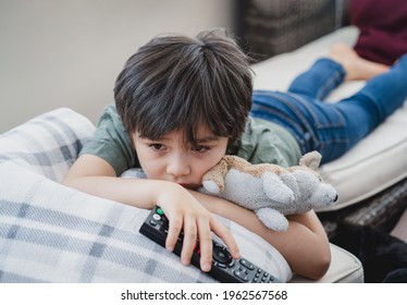 Dramatic Portrait Lonely Kid Sad Face Holding Remote Control Sitting On Couch,child Sitting On Sofa In Living Room With Looking Out Deep In Thought, Boy Bored Stay At Home Alone.