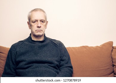 Dramatic Portrait Of A Sad And Depressed Adult Man Sit On A Sofa And  Looking Into Space With Lackluster Eyes. Negative Space For Copy Text