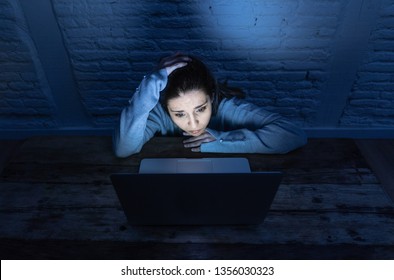 Dramatic portrait of sad scared young woman stressed and worried staring at laptop suffering cyber bullying and harassment. Victim of online abuse and intimidation by stalker. In dangers of internet.