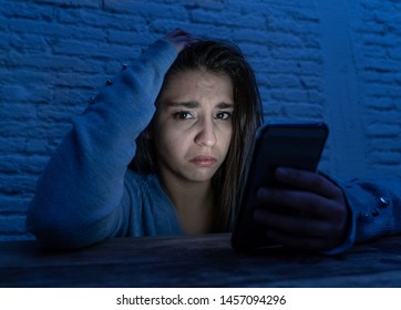 Dramatic Portrait Of Sad Scared Young Woman Victim Of Online Harassment And Cyberbullying. Looking At Smart Mobile Phone Stressed And In Fear Being Online Abused By Stalker. In Dangers Of Internet.