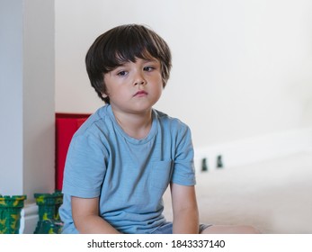 Dramatic portrait tired kid siting alone and lookig out deep in throught, Bored child siting on floor with unhappy face, Lonely Young boy with sad face sitting alone in corner, Health metal concept