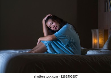 dramatic portrait of young beautiful and sad Asian Chinese woman crying desperate on bed awake at night suffering depression crisis and insomnia feeling pain and broken heart