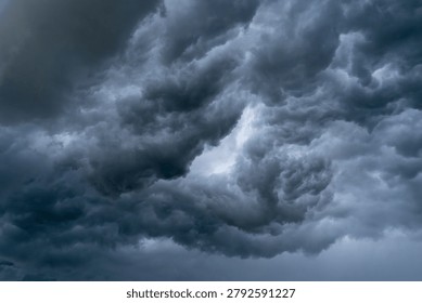 Dramatic and powerful cloudscape capturing a turbulent, brooding storm sky filled with dark, churning cumulonimbus clouds in dramatic shades of grey, charcoal and slate blue. The entire frame is consumed by the towering storm clouds, which build and billow with immense energy and movement, their swirling forms suggesting strong atmospheric turbulence and an imminent downpour or thunderstorm. The tonal range within the clouds is exceptional, moving from near-black at the densest, most threatening formations to lighter silvery grey at the edges where diffused light attempts to break through, creating a powerful chiaroscuro effect across the sky. There is no horizon, no land, no reference point — only the raw, elemental force of the storm filling the composition completely and demanding the viewer's full attention. The overall mood is intense, foreboding and awe-inspiring, conveying the full drama and power of extreme weather with cinematic impact. An exceptionally strong and versatile image suitable for weather and meteorology content, news and editorial use, dramatic background imagery, climate and environment campaigns, creative and conceptual design projects, film and music promotional material, and any project requiring a bold, moody and impactful visual statement.