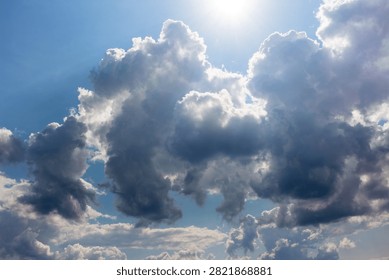 Dramatic puffy white clouds drifting across a bright blue sky with radiant sunlight piercing through the atmosphere creating a heavenly and peaceful nature vista on a sunny day