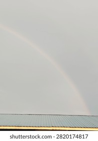 A dramatic rainbow emerging through dark storm clouds after rainfall, creating a striking contrast between vibrant colors and a moody overcast sky. A beautiful natural weather phenomenon symbolizing hope, renewal, and the calm after the storm. Ideal for nature, weather, climate, background, and inspirational concepts