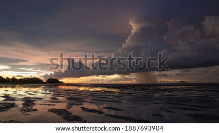 A dramatic raincloud during a beautiful tropical sunset over shallow water and a tropical island