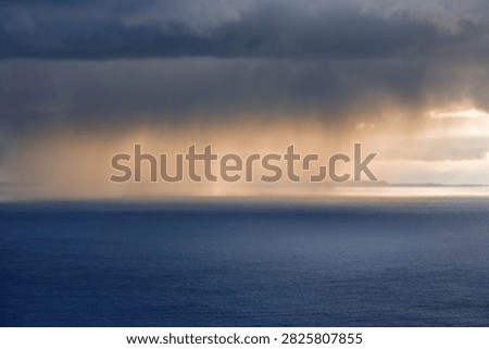 Dramatic rainstorm over calm ocean at sunset