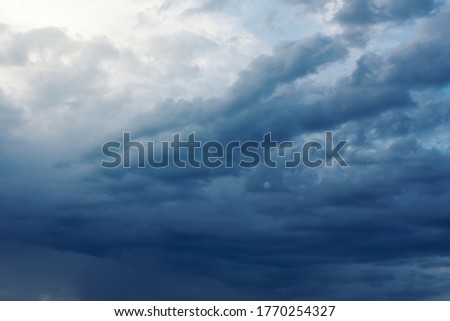 Dramatic rainy clouds on dark blue stormy evening sky. Natural background with stormclouds and sunlights of setting sun.