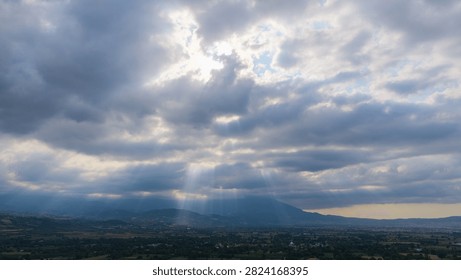 Dramatic rays of sunlight filtering through the clouds into the valley (the Tyndall effect). A magnificent photograph of the sky and landscape.