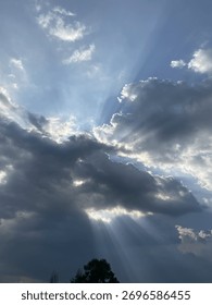 Dramatic rays of sunlight, known as crepuscular rays, pierce through a dense layer of dark, dramatic clouds, creating a powerful, celestial contrast in the sky.