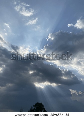 Dramatic rays of sunlight, known as crepuscular rays, pierce through a dense layer of dark, dramatic clouds, creating a powerful, celestial contrast in the sky.