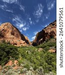 Dramatic red cliffs and lush greenery meet under wispy blue skies in Kolob Canyons, a stunning and less-crowded section of Zion National Park in southern Utah.