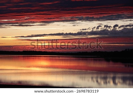 Dramatic red and orange sunset over Lac du Der with reflections on calm water, Champagne-Ardenne, France