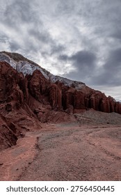 Dramatic red rock formations and canyons under a stormy overcast sky in a desert landscape. Low angle view.