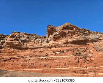 Dramatic red sandstone cliffs and exposed rock bed along the coastline of Hilbre Island at low tide under a bright blue sky, weathered red sandstone rock formations displaying natural erosion layers on the shore 